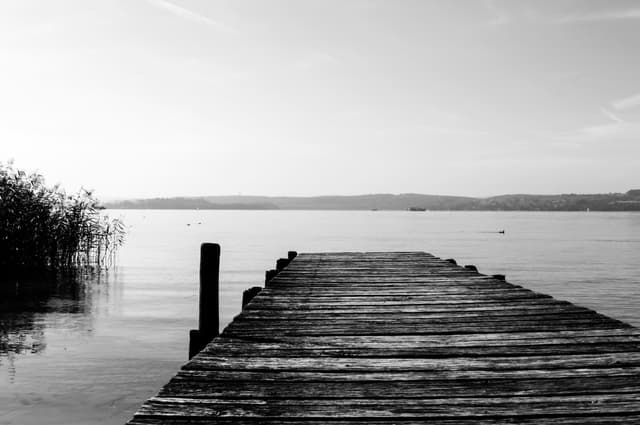 The end of a wooden bridge looking over a peaceful lake on a cloudy day